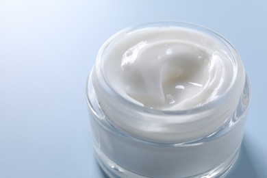 Photo of Face cream in jar on light blue background, closeup. Space for text