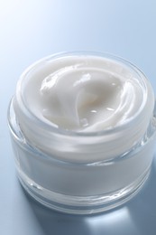 Photo of Face cream in jar on light blue background, closeup