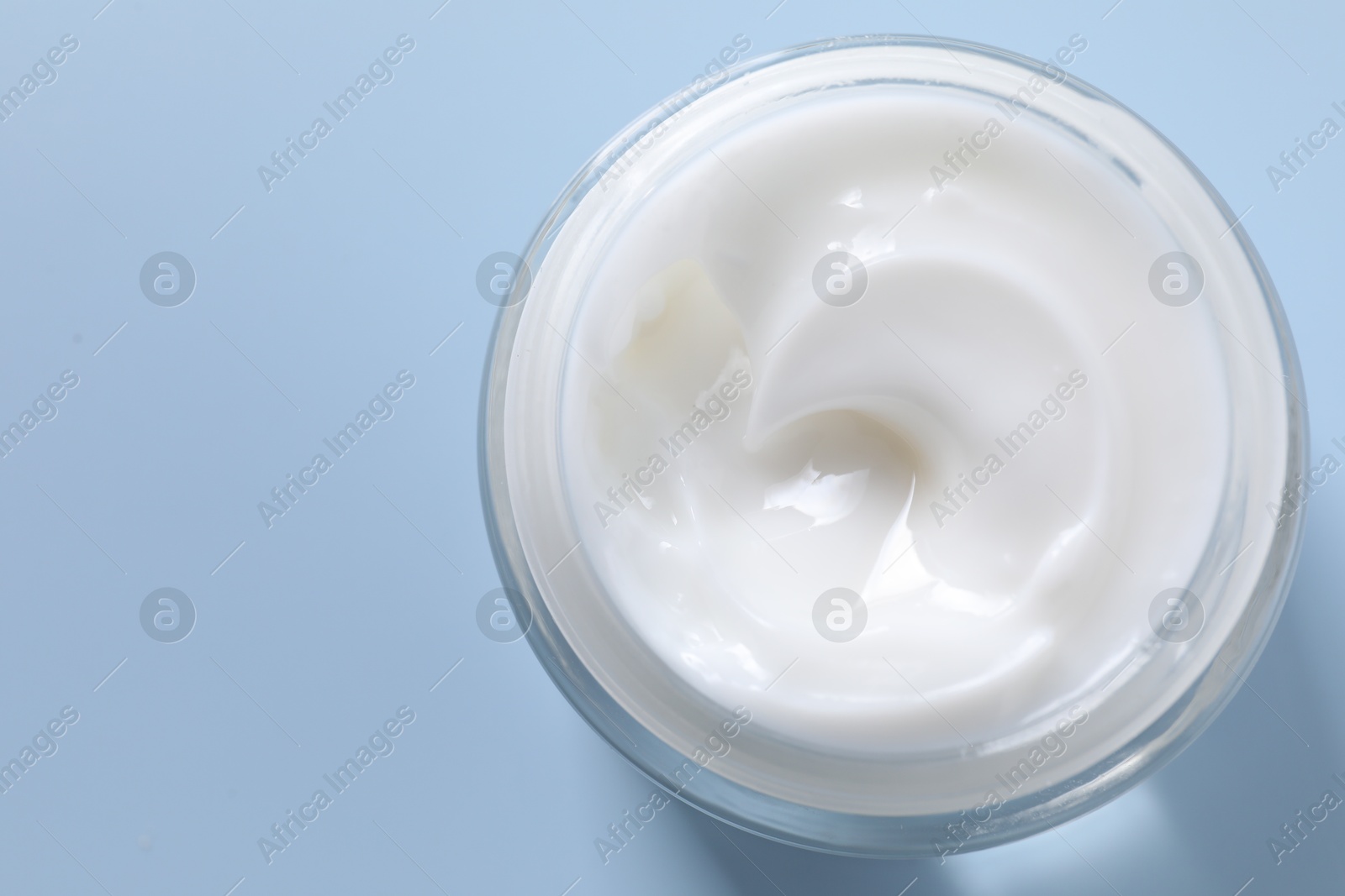 Photo of Face cream in jar on light blue background, top view. Space for text