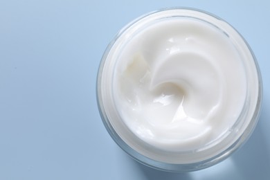 Face cream in jar on light blue background, top view. Space for text