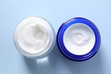 Face cream in jars on light blue background, flat lay