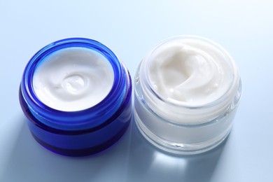 Face cream in jars on light blue background, closeup