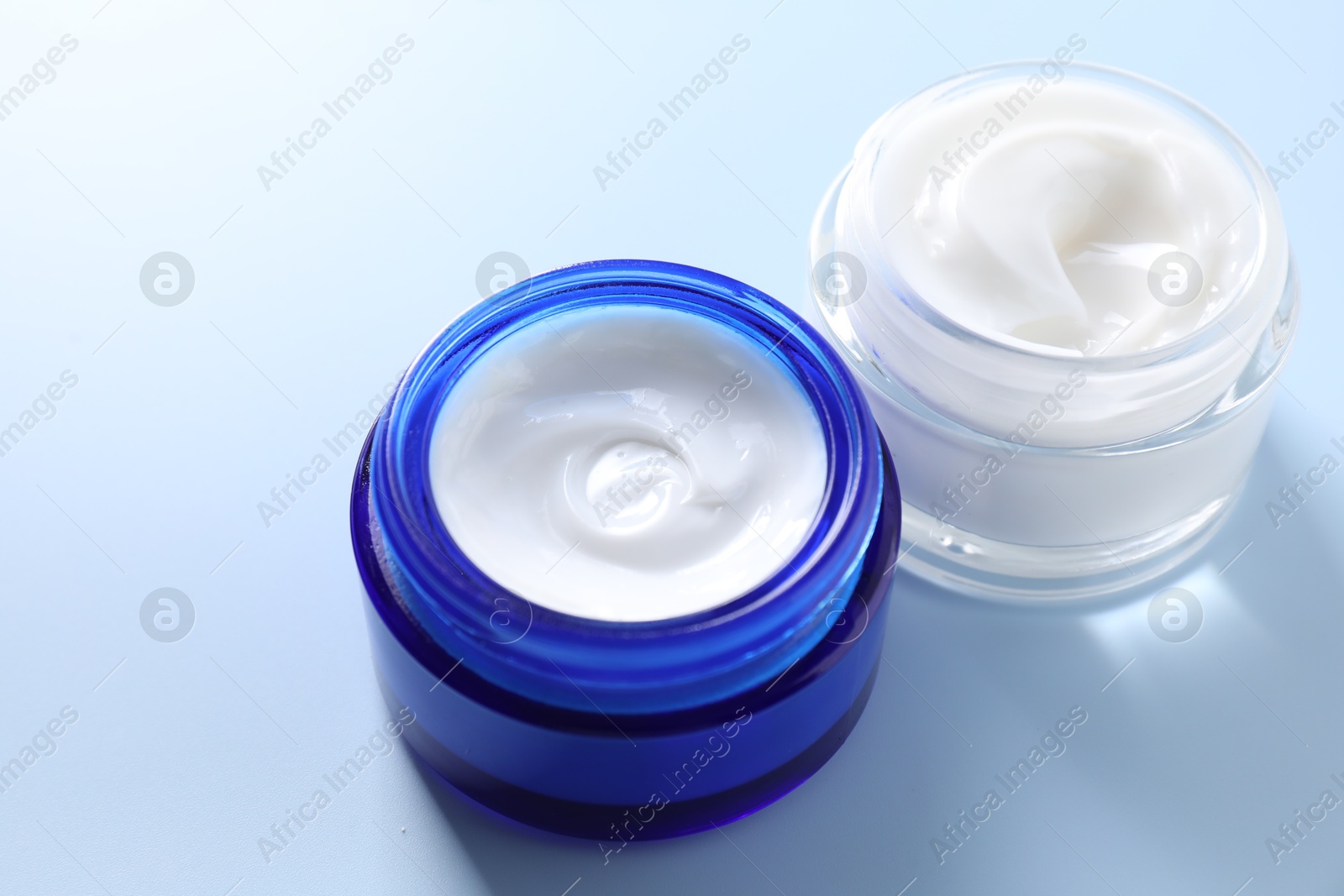 Photo of Face cream in jars on light blue background, closeup