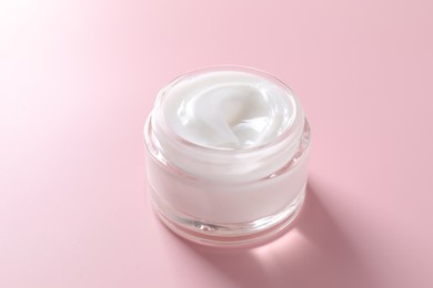 Face cream in jar on pink background, closeup