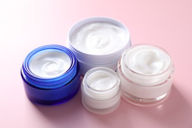 Face cream in jars on pink background, closeup