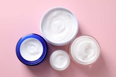 Face cream in jars on pink background, flat lay