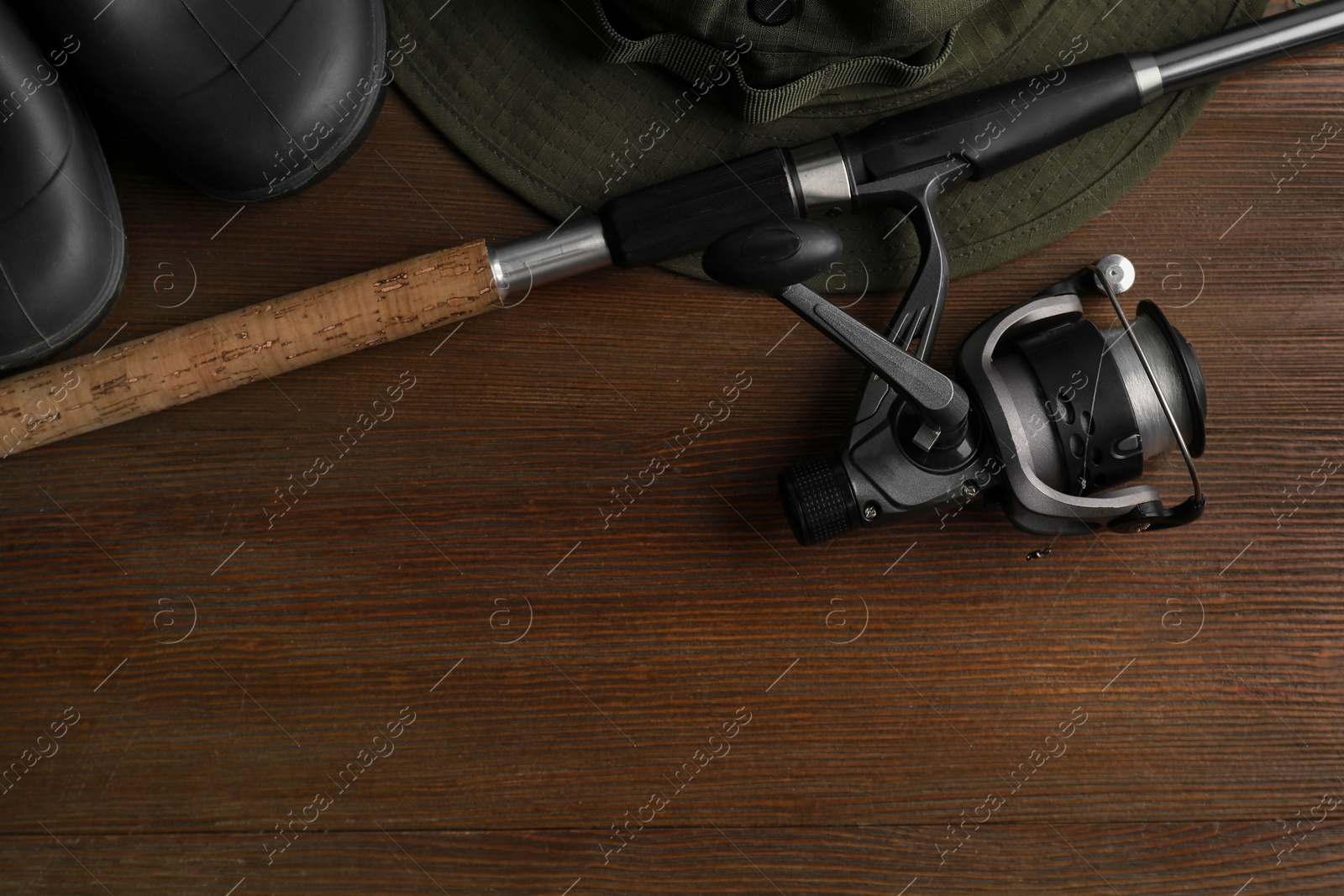 Photo of Fishing rod with spinning reel, hat and boots on wooden table, top view. Space for text