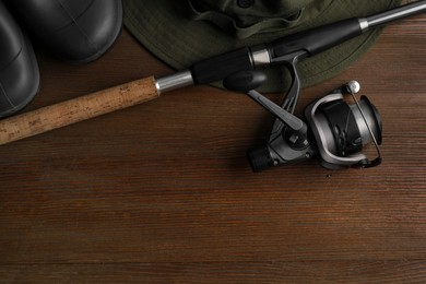 Fishing rod with spinning reel, hat and boots on wooden table, top view. Space for text