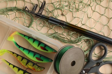 Photo of Fishing rod, baits, line, scissors and net on wooden table, top view