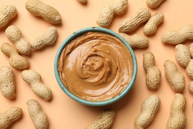 Photo of Tasty peanut butter in bowl and groundnuts on beige background, flat lay