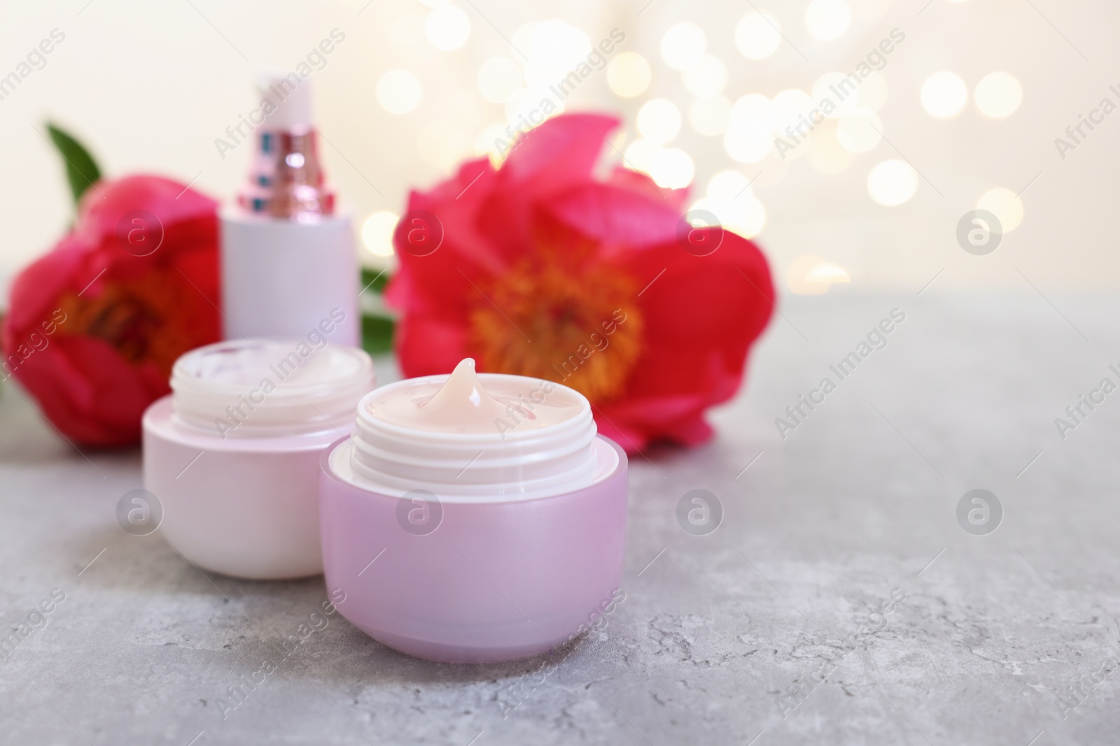 Photo of Set of different cosmetic products and peony flower on gray table against light background with blurred lights. Space for text