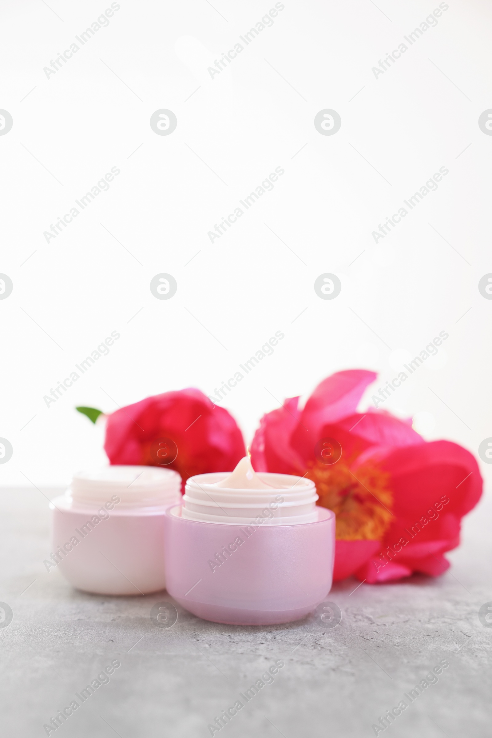 Photo of Jars of creams and peony flower on gray table against light background, closeup. Space for text