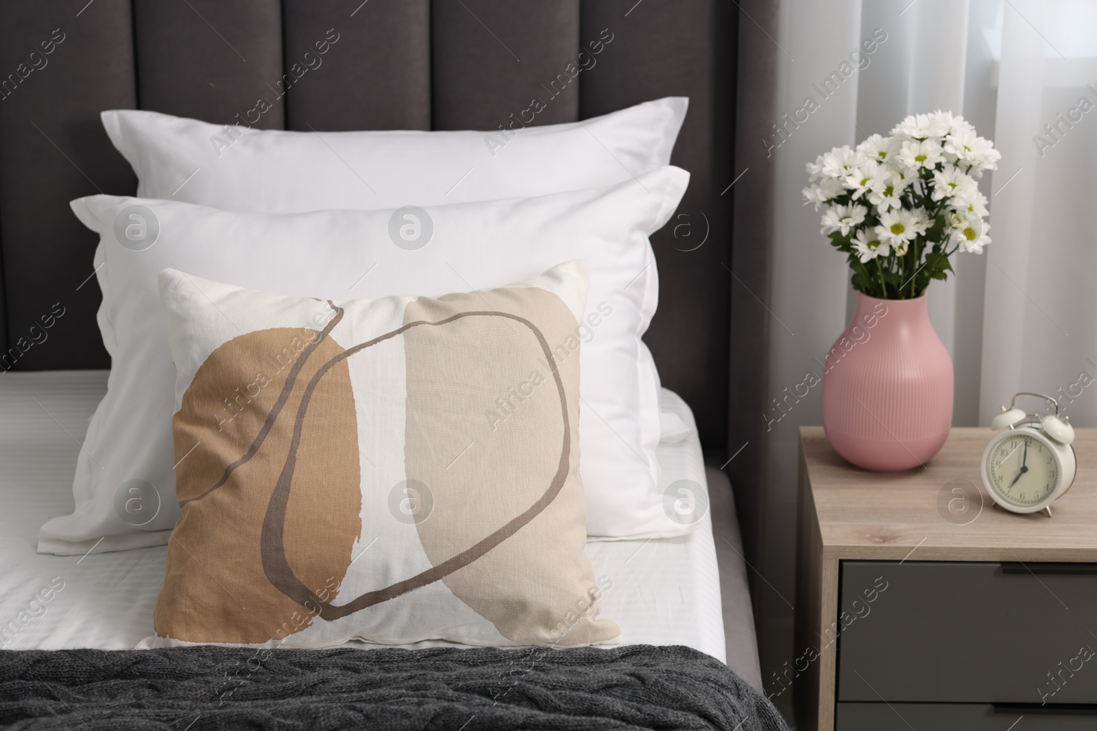 Photo of Many soft pillows on bed and bedside table with flowers at home, closeup