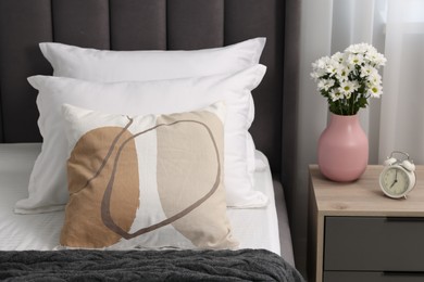 Many soft pillows on bed and bedside table with flowers at home, closeup