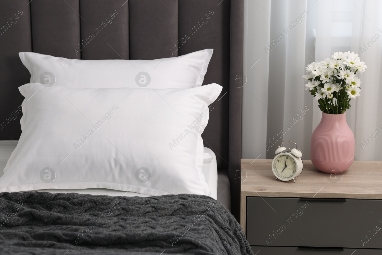 Photo of Many soft pillows on bed and bedside table with flowers at home, closeup