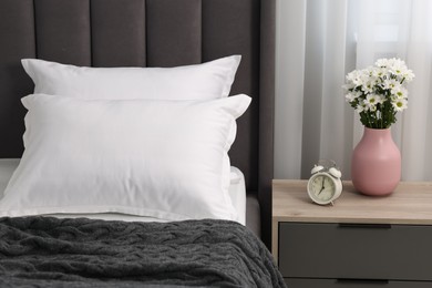 Many soft pillows on bed and bedside table with flowers at home, closeup