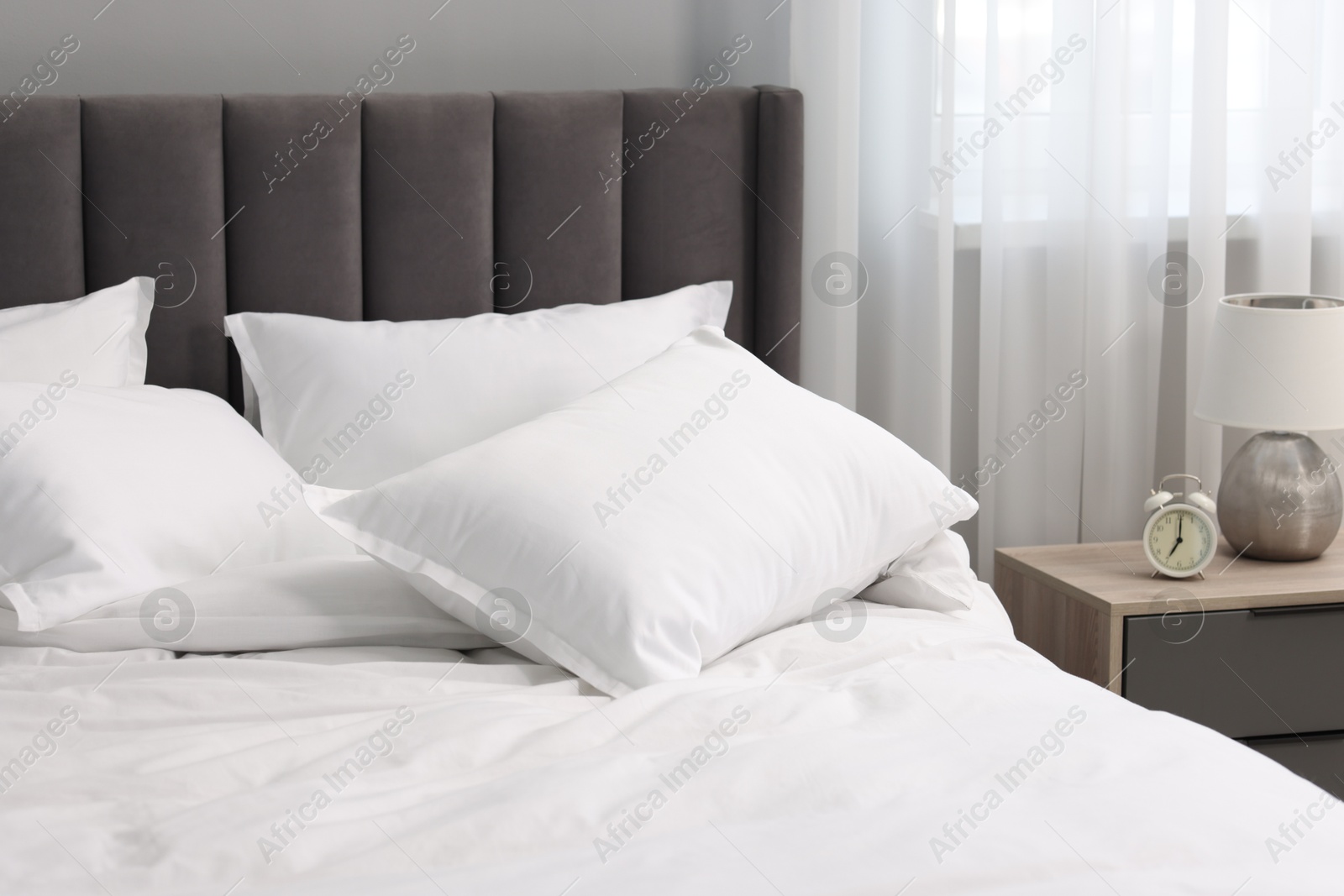 Photo of Many soft pillows on bed and bedside table at home