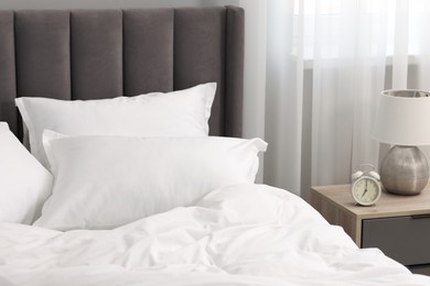 Photo of Many soft pillows on bed and bedside table at home