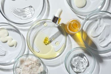 Photo of Petri dishes with different cosmetic products on white background, flat lay