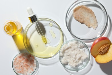 Petri dishes with different cosmetic products and peach on white background, flat lay