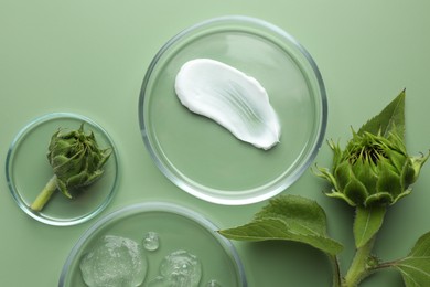 Photo of Petri dishes with cosmetic products and sunflowers on green background, flat lay