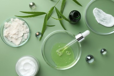 Photo of Petri dishes with cosmetic products, pipette and leaves on green background, flat lay