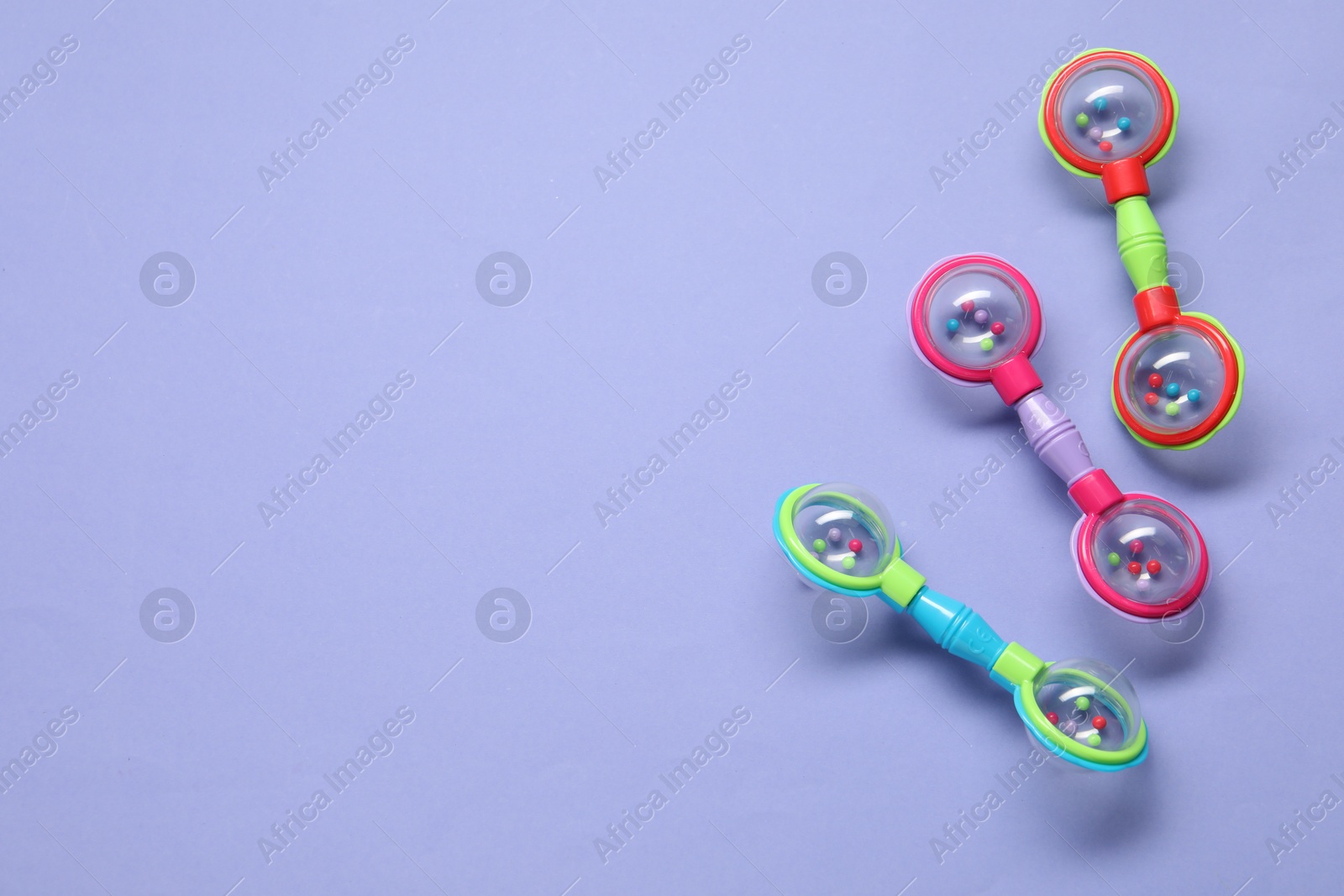 Photo of Colorful rattles on violet background, flat lay with space for text. Baby accessories