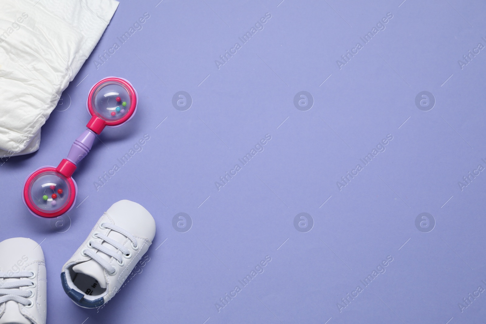 Photo of Colorful rattle, diaper and baby shoes on violet background, flat lay. Space for text