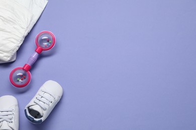 Colorful rattle, diaper and baby shoes on violet background, flat lay. Space for text