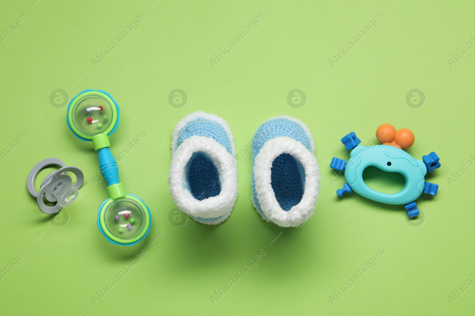 Photo of Colorful rattles, knitted booties and pacifier on green background. Baby accessories