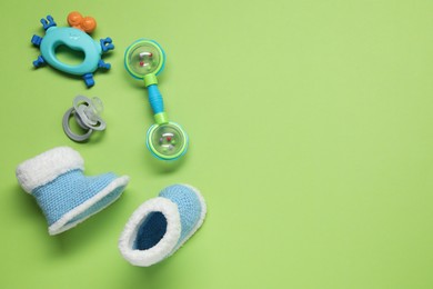 Photo of Colorful rattles, knitted booties and pacifier on green background with space for text. Baby accessories