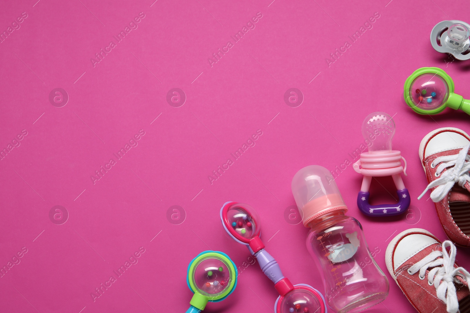 Photo of Colorful rattles, bottle, baby shoes and pacifiers on pink background, flat lay. Space for text