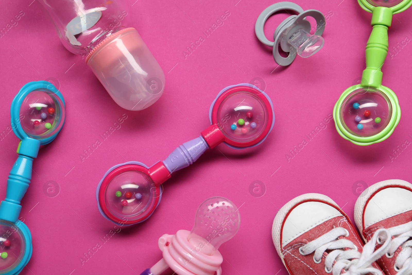 Photo of Colorful rattles, bottle, baby shoes and pacifiers on pink background, flat lay