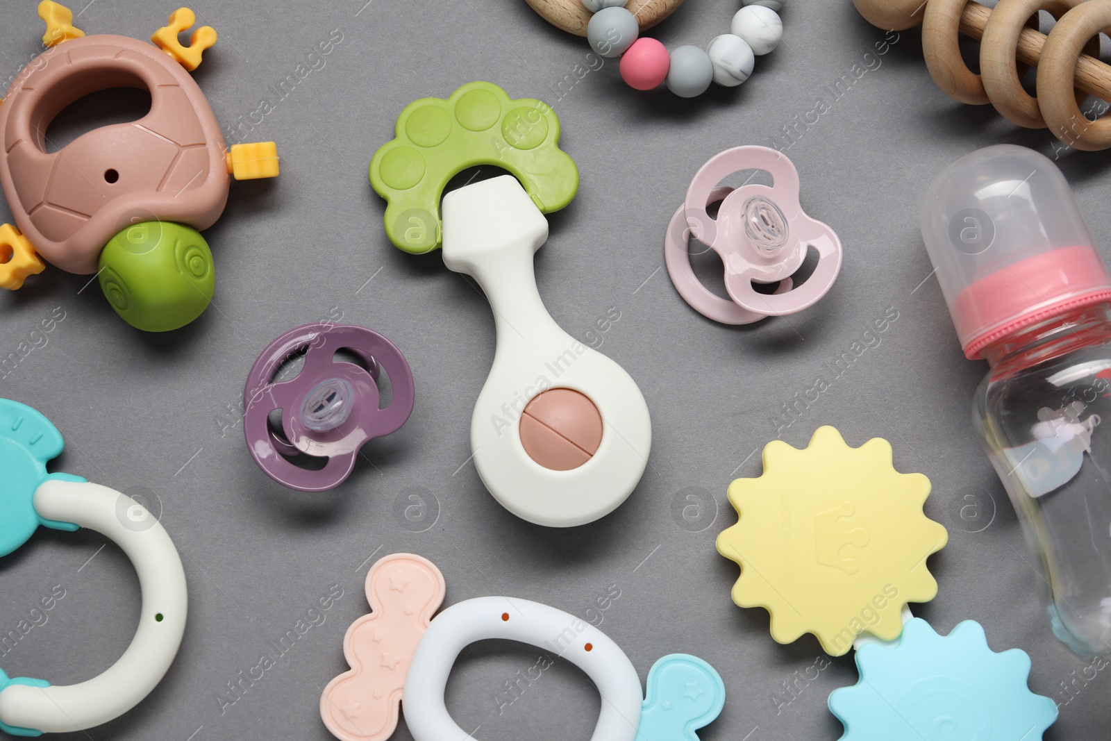 Photo of Colorful rattles, bottle and pacifiers on gray background, flat lay. Baby accessories