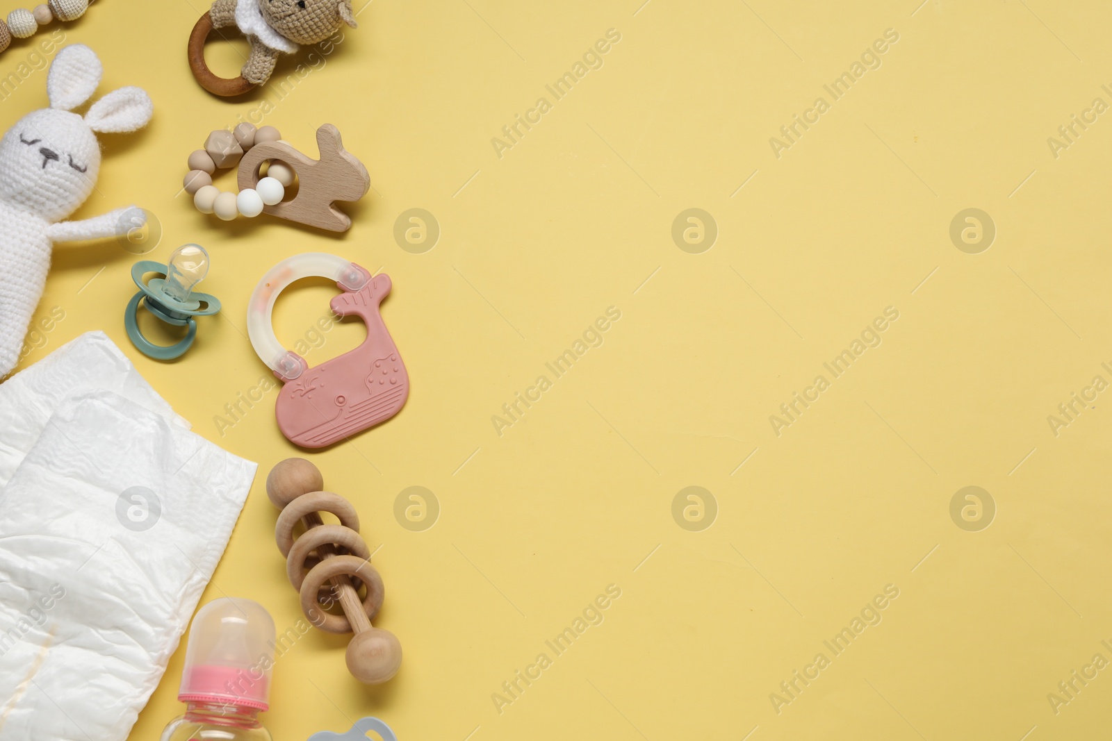 Photo of Colorful rattles, diapers, bottle and pacifiers on yellow background, flat lay with space for text. Baby accessories