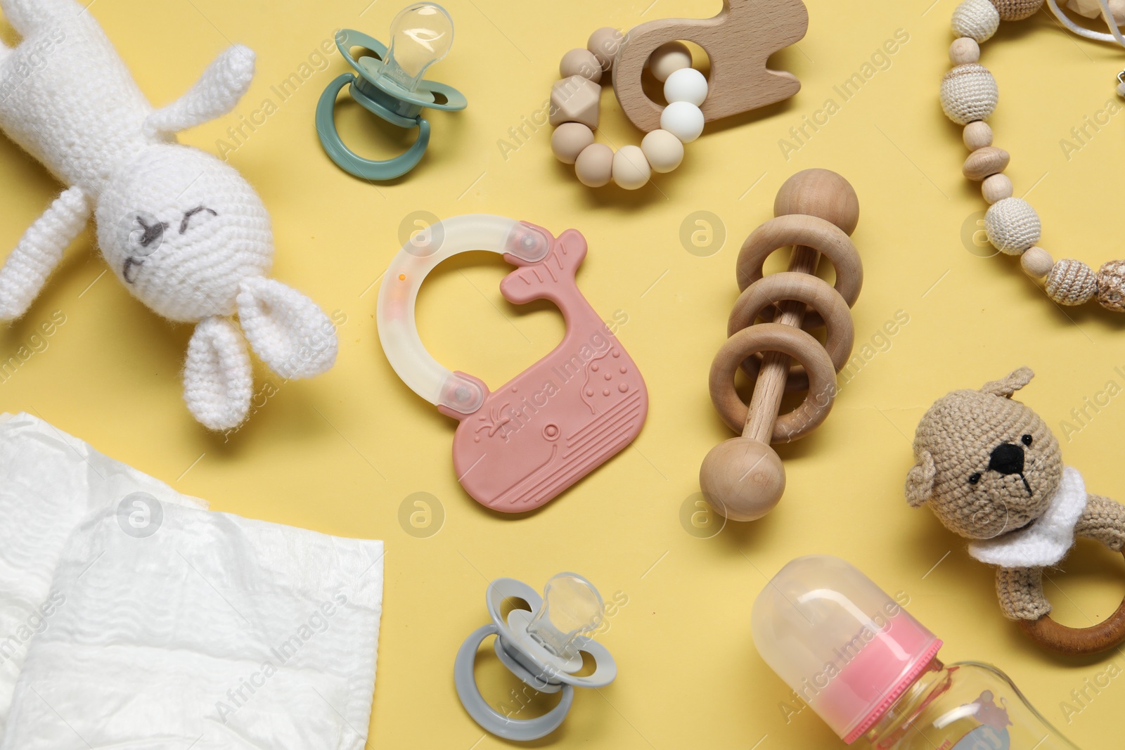 Photo of Colorful rattles, diapers, bottle and pacifiers on yellow background, flat lay. Baby accessories