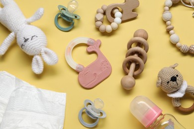 Colorful rattles, diapers, bottle and pacifiers on yellow background, flat lay. Baby accessories