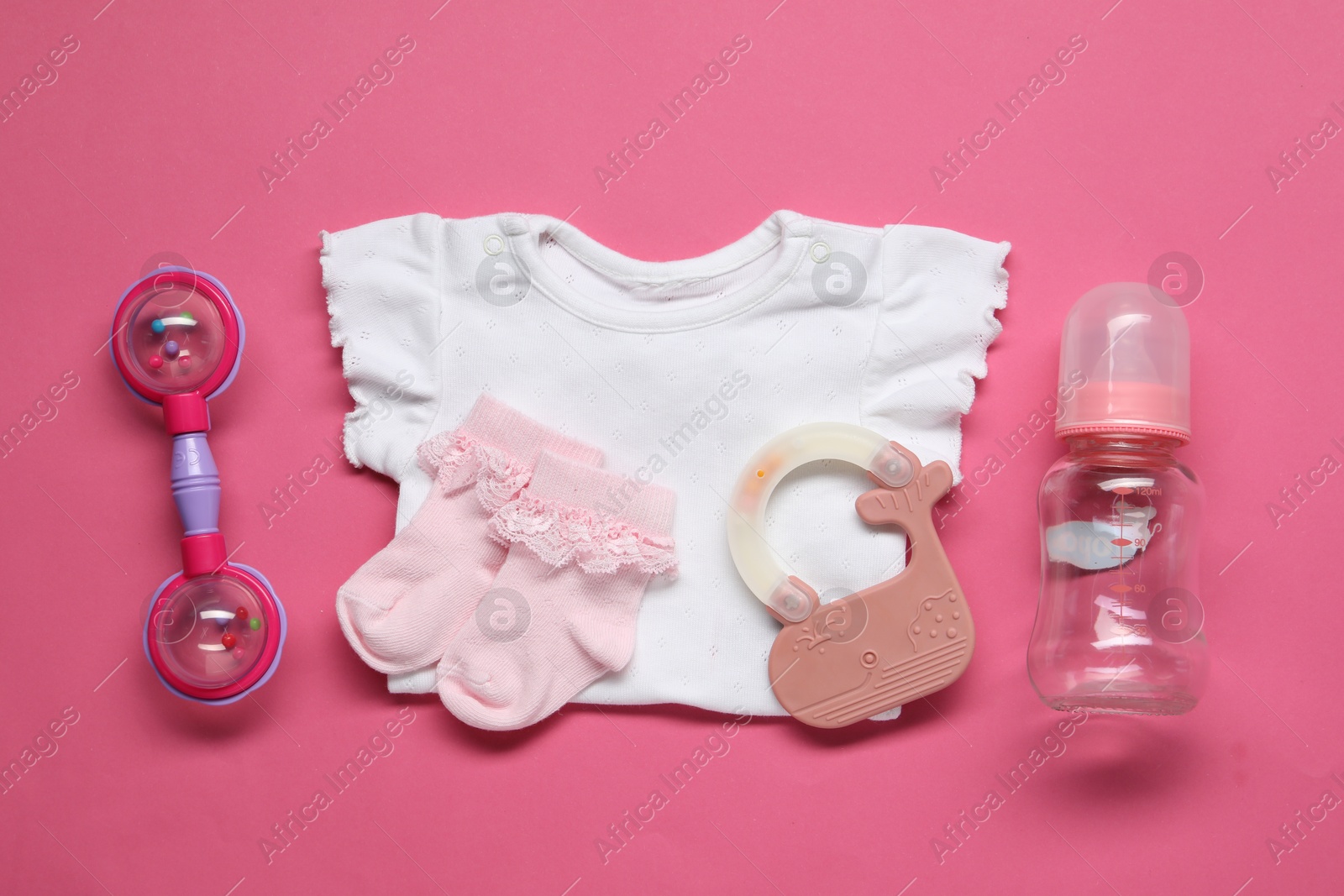 Photo of Colorful rattles and baby clothes on pink background, flat lay