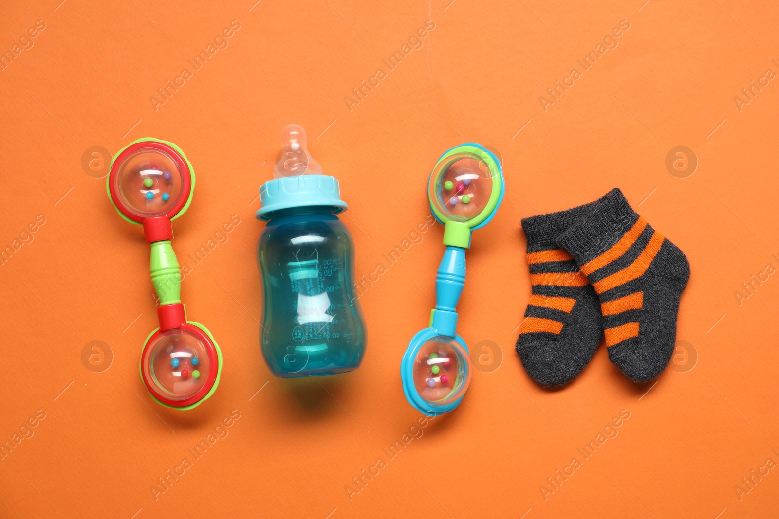 Photo of Colorful rattles, bottle and socks on orange background, flat lay. Baby accessories