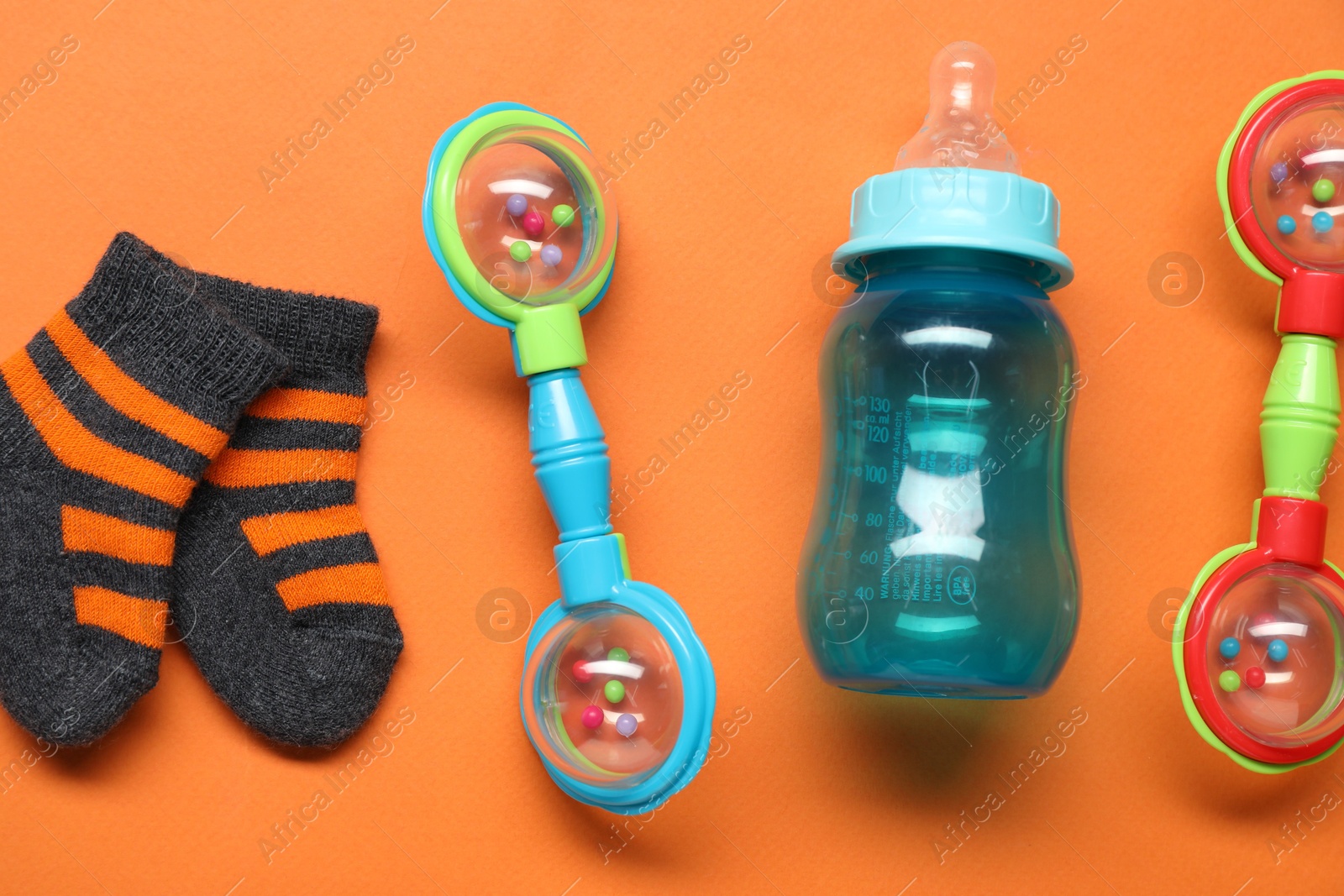 Photo of Colorful rattles, bottle and socks on orange background, flat lay. Baby accessories