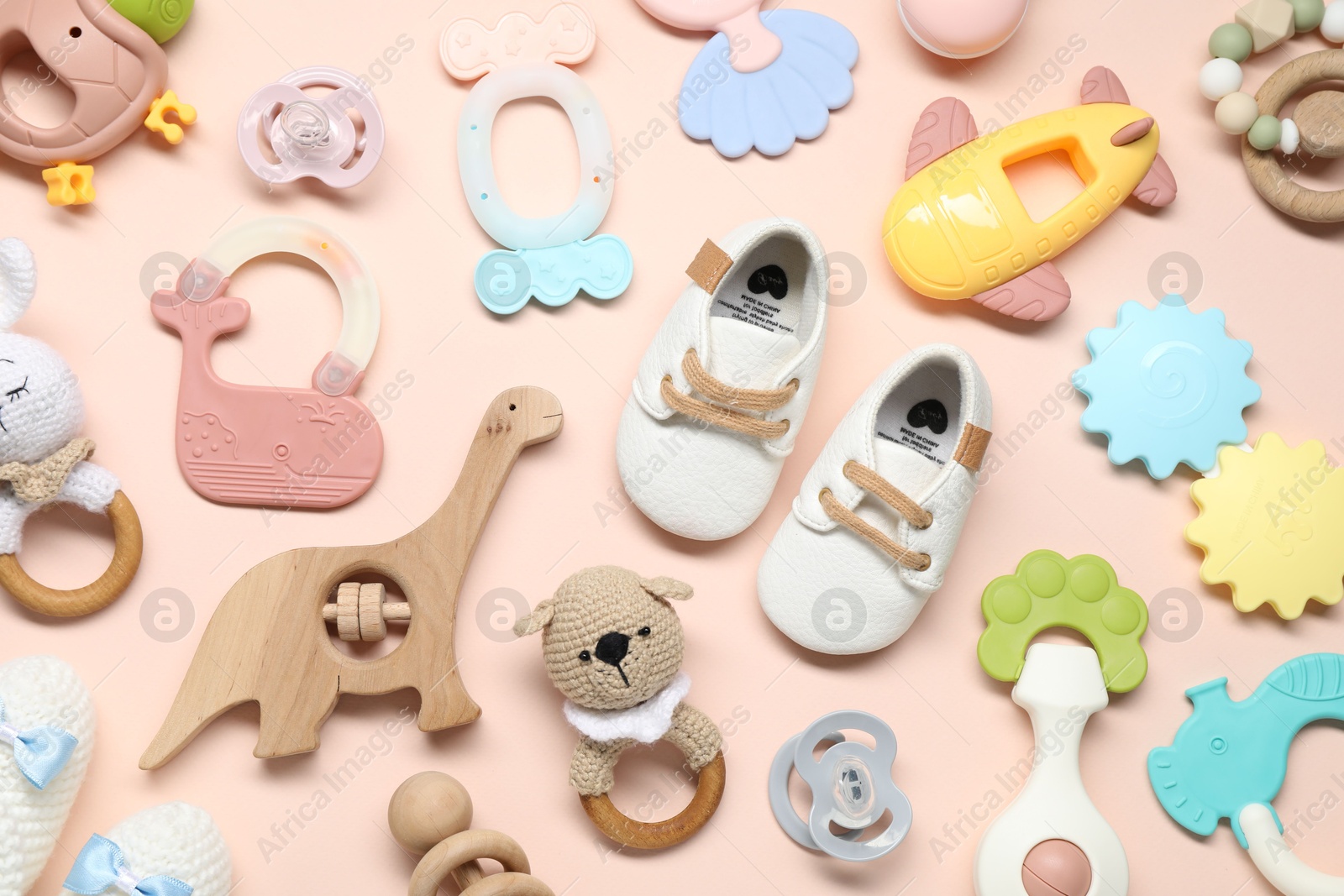 Photo of Colorful rattles, baby shoes and pacifiers on beige background, flat lay