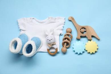 Wooden rattles, baby shirt and knitted booties on light blue background, flat lay