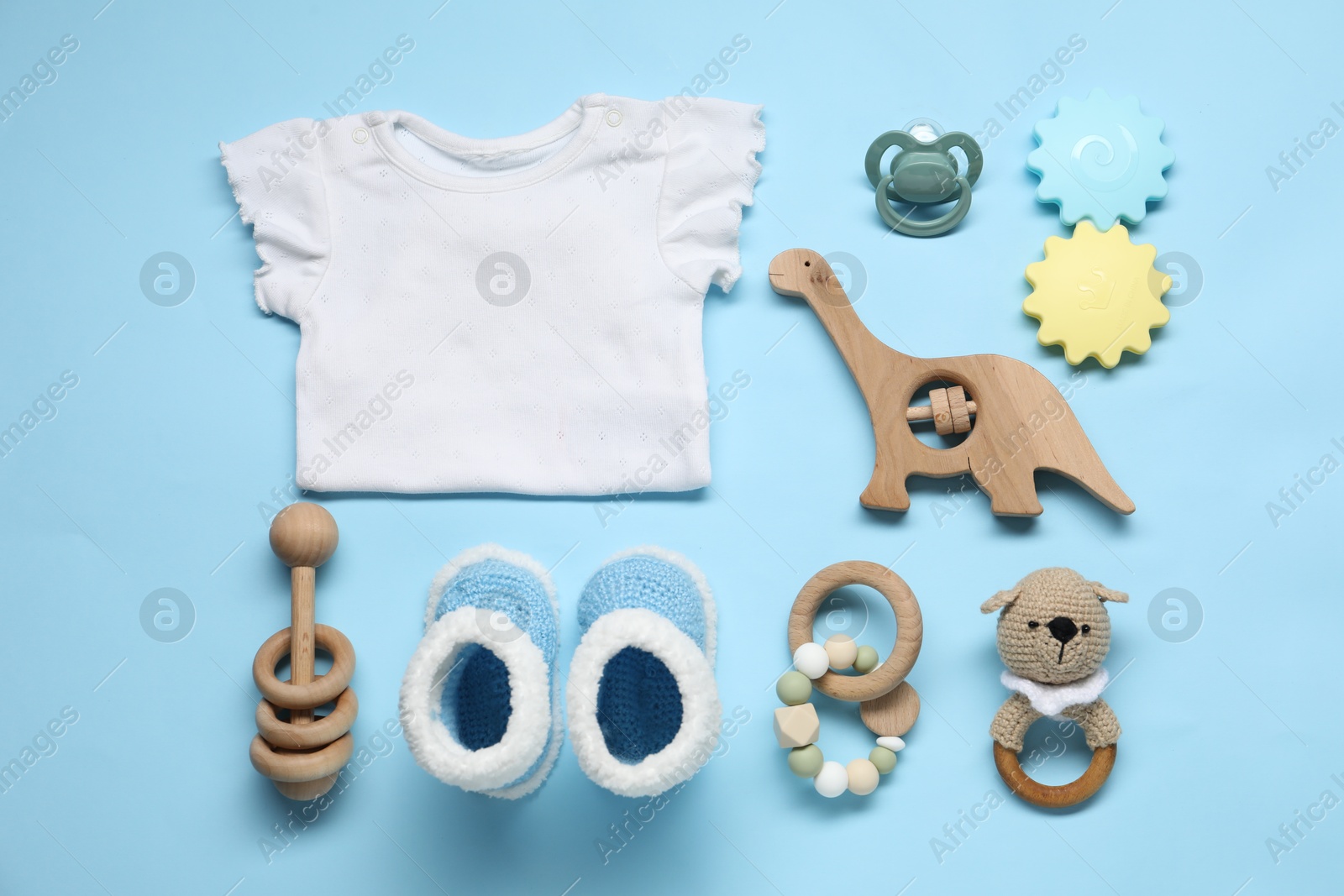 Photo of Wooden rattles, baby shirt and knitted booties on light blue background, flat lay