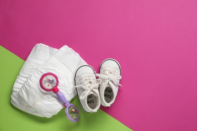 Baby rattle, booties and diapers on color background, top view. Space for text