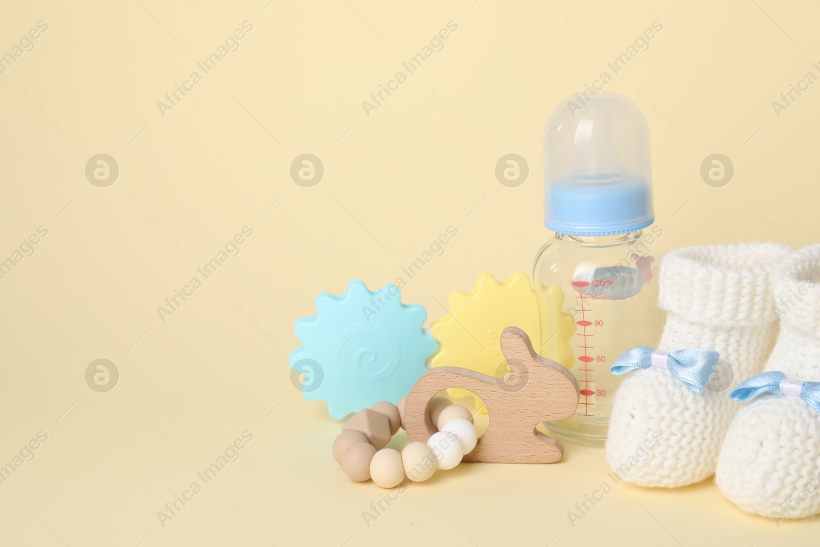 Photo of Baby toys, booties and bottle on beige background. Space for text