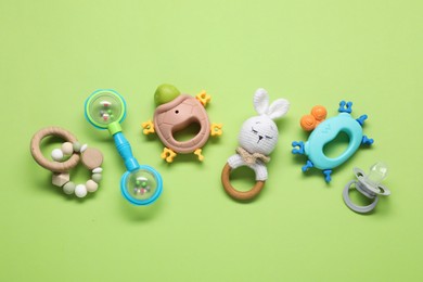 Different baby rattles on green background, flat lay