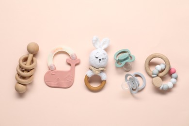 Different rattles and pacifiers on light pink background, flat lay