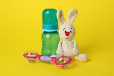 Baby rattle, toy bunny and bottle on yellow background