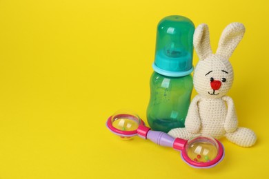 Baby rattle, toy bunny and bottle on yellow background. Space for text