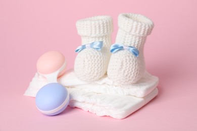 Photo of Baby rattle, booties and diapers on pink background